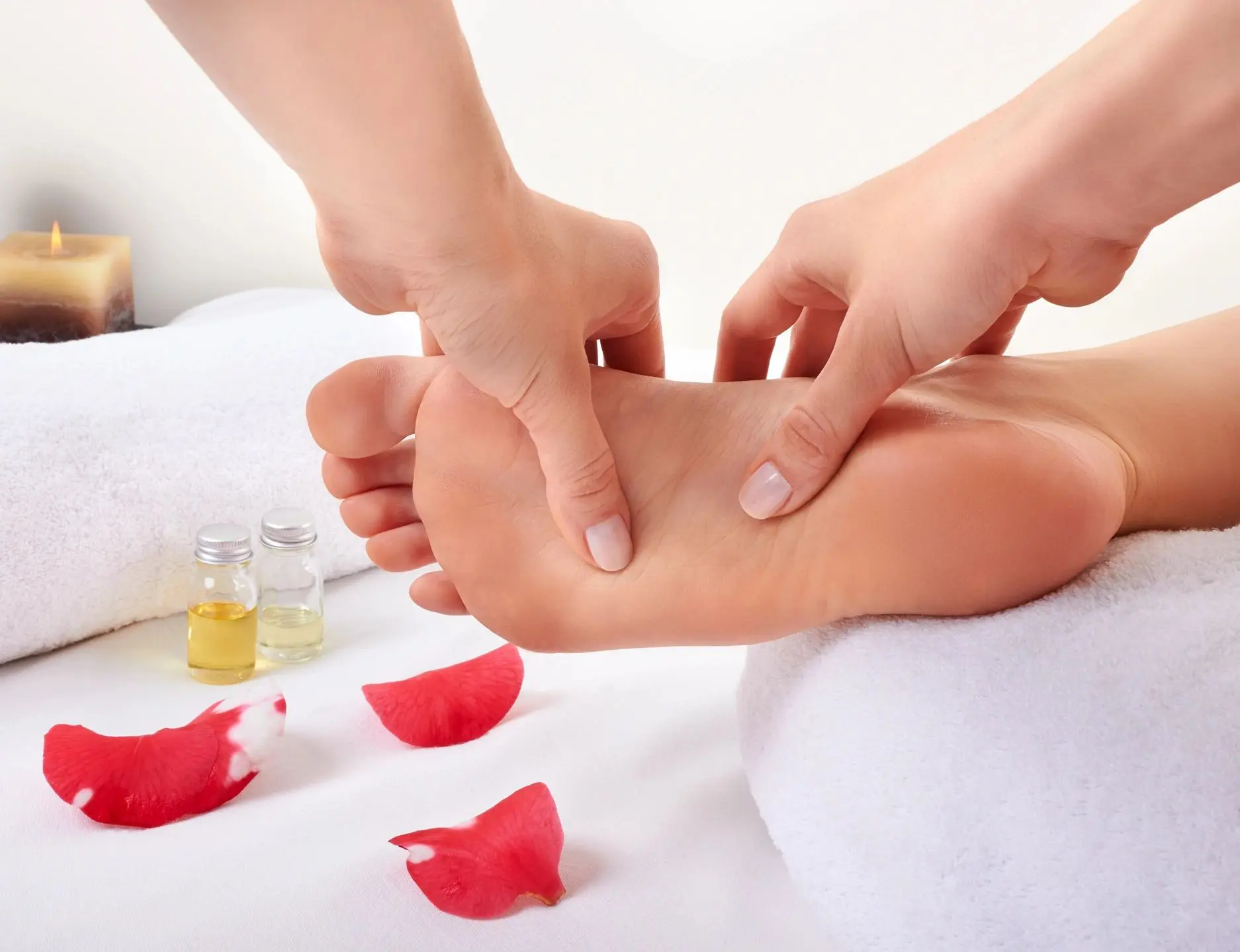 Hands massaging a foot with rose petals scattered nearby.